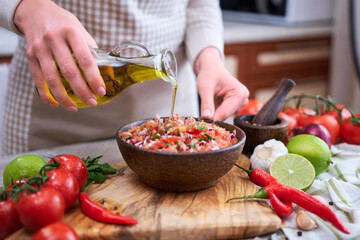 making salsa dip sauce - woman pouring olive oil to wooden bowl with chopped ingredients