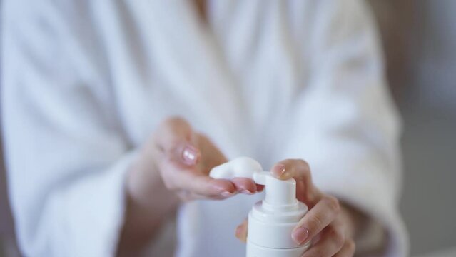 Beautiful young woman applying cleansing foam onto face in bathroom