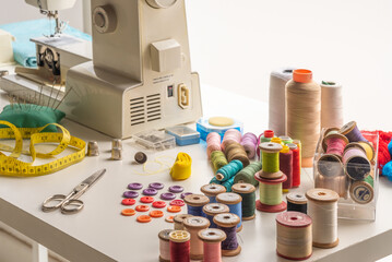 work table with spools of thread or bobbins. next to it, scissors and a tape measure, in the background, a sewing machine
