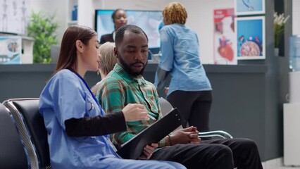 Diverse people talking about disease diagnosis in waiting room at hospital reception lobby. Man and woman doing checkup consultation to help with treatment and healthcare recovery. Handheld shot.