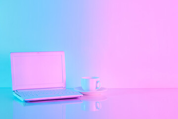 Office table with notebook computer and cup of coffee in vibrant gradient holographic neon colors...