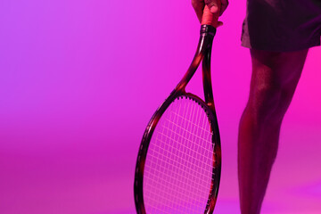 Image of low section of african american male tennis player in violet and pink neon lighting - Powered by Adobe