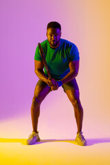 Fototapeta na wymiar Vertical image of african american male tennis player in violet and yellow neon lighting
