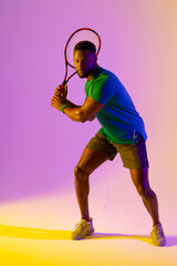 Vertical image of african american male tennis player in violet and yellow neon lighting