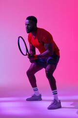 Vertical image of african american male tennis player in neon pink lighting