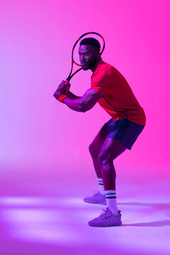 Vertical image of african american male tennis player in neon pink lighting