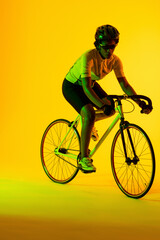 Obraz na płótnie Canvas Vertical image of african american female cyclist riding bike in yellow lighting