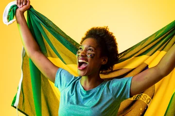 Fotobehang Image of african american female soccer fan with flag of brazil cheering in yellow lighting © vectorfusionart
