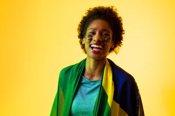 Fotobehang Image of african american female soccer fan with flag of brazil cheering in yellow lighting © vectorfusionart
