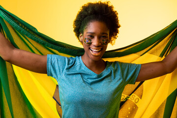 Image of african american female soccer fan with flag of brazil cheering in yellow lighting
