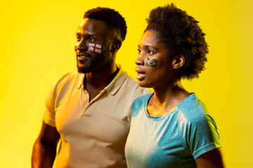 Image of african american soccer fan couple with flags of portugal and england in yellow lighting