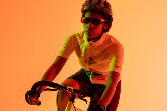 Image of african american female cyclist riding bike in neon orange lighting