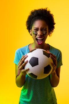 Vertical image of african american female soccer fan with flag of brazil in yellow lighting