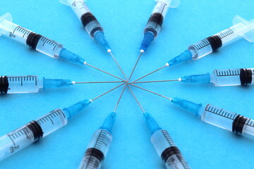 Many disposable syringes lie on a blue background.