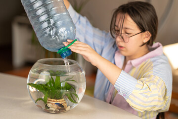 the girl changes the water in the aquarium. a girl pours clean water from a bottle into an aquarium