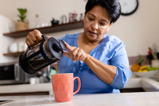 Low Angle View Of Biracial Mature Woman Pouring Coffee With French Press In Mug On Kitchen Island