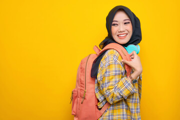 Side view. smiling young Asian Muslim woman student in plaid shirt with headphones and backpack isolated on yellow background. Education school university college concept