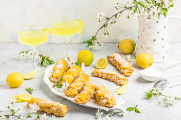 Eclairs with lemon curd topping on serving plate with glass of limoncello on a light background, concept of Italian and French cuisine, top view