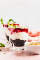 Cherry, cream cheese and chocolate biscuit portion layered dessert in glass, pink background. Black forest trifle. Summer dessert.