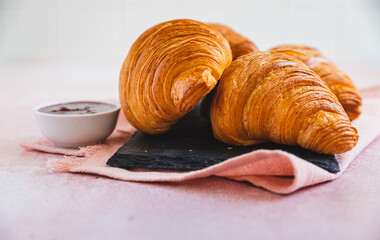 Fresh crispy croissants with red berry jam on black board, pink background. French croissant. Homemade bakery for tasty breakfast.