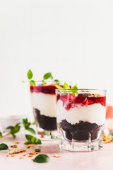 Cherry, cream cheese and chocolate biscuit portion layered dessert in glass, pink background. Black forest trifle. Summer dessert.
