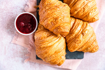 Fresh crispy croissants with red berry jam on black board, pink background. French croissant. Homemade bakery for tasty breakfast.
