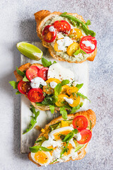 Variety of croissant sandwiches with tomato, cucumber, mozzarella cheese, eggs and mashed avocado with mint and arugula. Open savory sandwiches. Tasty healthy breakfast.