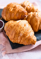 Fresh crispy croissants with red berry jam on black board, pink background. French croissant. Homemade bakery for tasty breakfast.