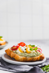 Variety of croissant sandwiches with tomato, cucumber, mozzarella cheese, eggs and mashed avocado with mint and arugula. Open savory sandwiches. Tasty healthy breakfast.