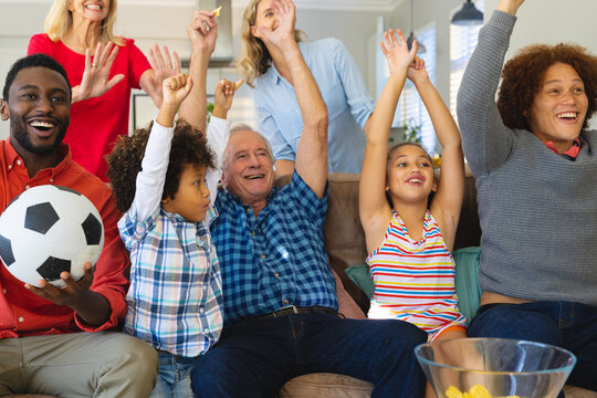 Multigeneration multiracial family with arms raised celebrating victory while enjoying soccer match