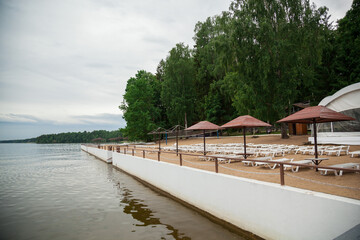 Sandy beach with sun beds and umbrellas by the pond.