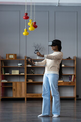 African American young woman using Vr reality headset, playing in 3d virtual game at home. Technology digital futuristic innovation device concept. Happy Black girl enjoy vr gaming in living room © DimaBerlin
