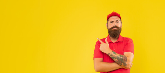 Fototapeta premium Serious bearded man in casual red cap and tshirt pointing finger aside copy space, advertise