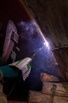 Working person welding a metal with a welding machine.
