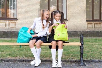 two school girls sit on bench with backpack together. knowledge day