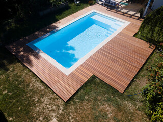 Drone flight over pool with nice wooden terrace surrounded by green lawn in beautiful garden