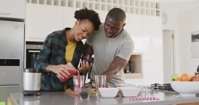 Video of happy african american couple preparing juice together in kitchen