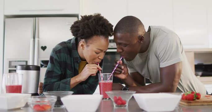 Video of happy african american couple drinking homemade juice from one glass with straws