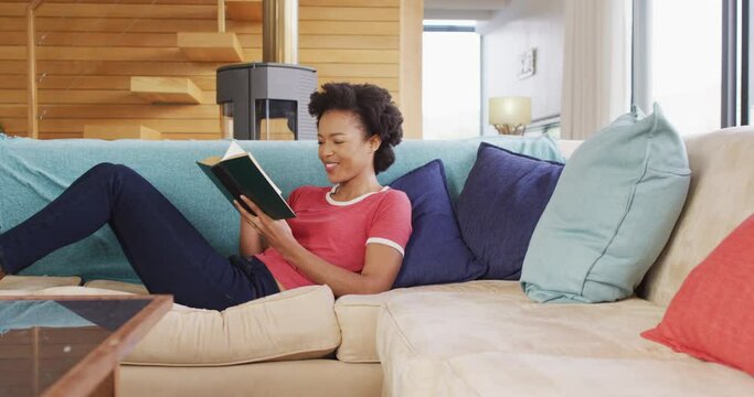 Video of african american woman reading book on sofa