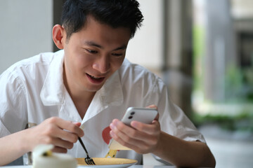 Fototapeta na wymiar happy Asian young man check phone while eating