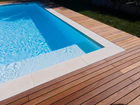 Drone flight over pool with nice wooden terrace surrounded by green lawn in beautiful garden