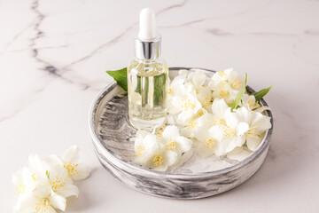 Obraz na płótnie Canvas natural jasmine oil in a glass bottle with a pipette on a round plaster tray with white flowers of the plant. organic self-care.