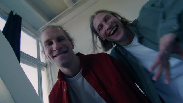 Close-up portrait of Caucasian twin brothers looking at camera and smiling. Two positive young men posing at home. Friendship, family, identical siblings.
