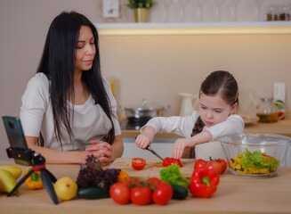 Happy mother and daughter enjoy prepare freshly salad together in kitchen. Healthy food at home. Healthy Lifestyle and Eating Concept. little influencer filming blog about healthy eating