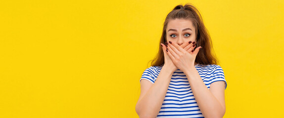 Scared girl in white-blue striped t shirt covers mouth hands and looking at camera with shocked...