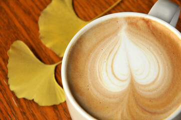 cup of coffee on wooden table and ginkgo leaf