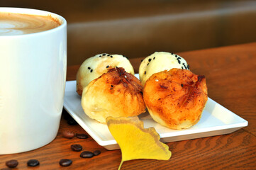cup of coffee with fried buns and ginkgo leaf on wooden table