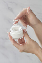 Close up of woman's hand is taking cream from a jar with her finger. Use of cosmetics with natural ingredients for clean and soft skin. Healthcare, skin care and beauty  concept.