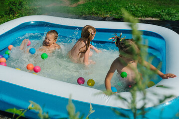 Happy cute children, preschoolers, bathe in the summer in the village in inflatable pool, make splashes. Siblings, kids having fun together. Children playing and swimming in water on the backyard.
