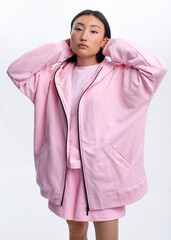 Fototapeta premium Beautiful Asian girl in a pink casual tracksuit posing against a white wall in a photo studio